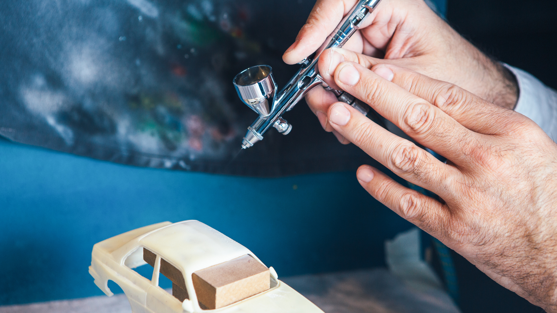 Person spray painting a scale model of a car with an airbrush.